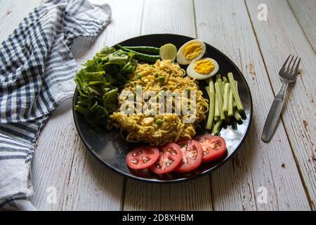 Gros plan des nouilles instantanées avec les ingrédients alimentaires dans une plaque noire Banque D'Images