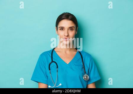 Concept de covid-19 et concept de quarantaine. Gros plan d'une jeune femme médecin confiante avec stéthoscope, portant des gommages, debout sur fond bleu Banque D'Images