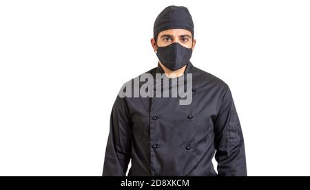 Chef à l'époque des coronavirus. Jeune cuisinier avec un masque de protection du visage en tissu noir isolé sur fond blanc. COVID19 sécurité dans la cuisine restaurant nourriture pr Banque D'Images