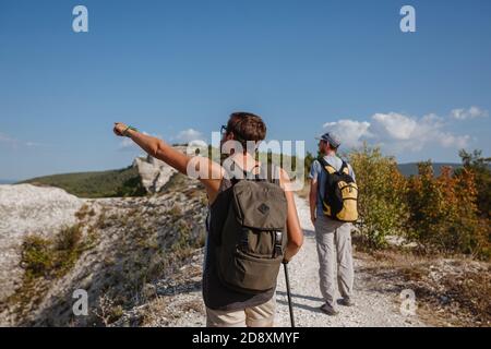 Deux randonneurs avec des sacs à dos et d'autres engins d'escalade restant au sommet du rocher. Homme pointant avec sa main discutant de la route. Plan, vision et mission concep Banque D'Images