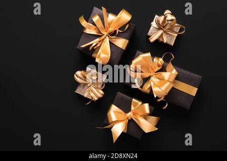 Boîtes-cadeaux dorées emballées de façon festive sur fond noir. Style de pose à plat. Concept des fêtes et du Vendredi fou Banque D'Images
