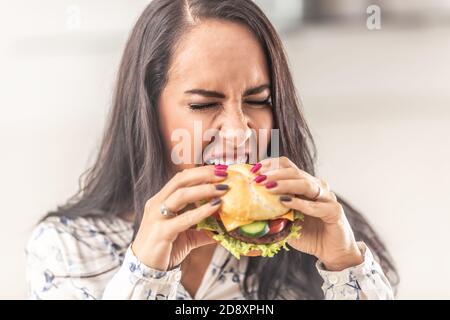 Fille essayant d'ouvrir la bouche autant que possible pour un gros hamburger. Banque D'Images