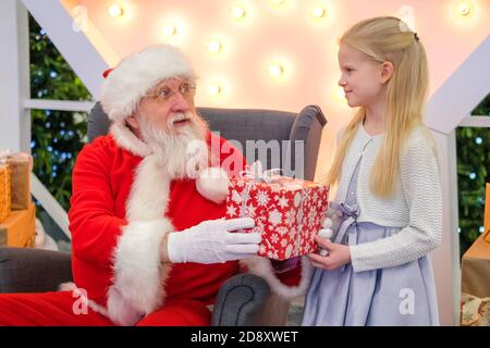 Le Père Noël offre un cadeau à une fille dans le centre commercial. Vrai Père Noël authentique parler et jouer à des jeux surprise avec des enfants . Ventes et souhaits de Noël Banque D'Images