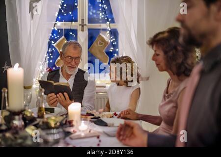 Homme âgé avec une famille étendue à l'intérieur célébrant Noël, lisant la Bible. Banque D'Images