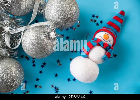 Bonhomme de neige feutré de Noël et du nouvel an en bonnet tricoté bleu rouge sur fond bleu avec ornements de noël argentés. Décoration, jouets et cadeaux Banque D'Images