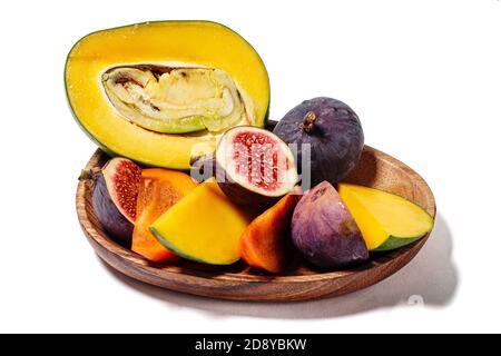 Portion de mangue en tranches, de persimmon et de figues sur un plat de bois isolé sur blanc Banque D'Images