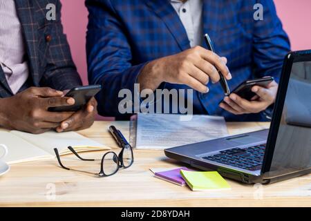 Gros plan court de deux hommes portant des costumes assis au bureau, sur un ordinateur portable et un smartphone. Journée de travail au bureau. Mise au point sélective. Lunettes, n Banque D'Images