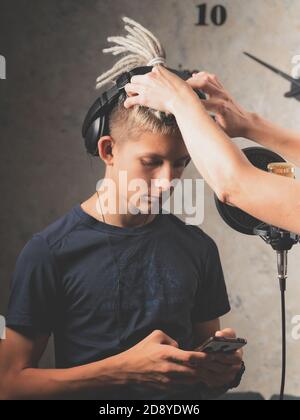 Le styliste corrige la coiffure du jeune chanteur pendant l'enregistrement en studio. Tir vertical Banque D'Images