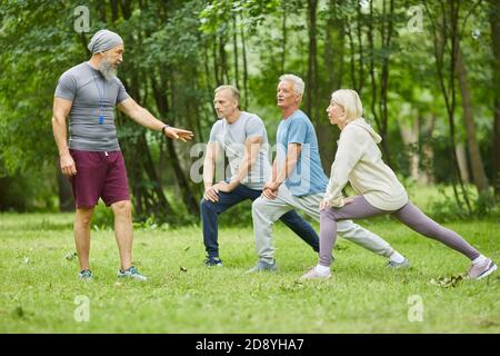 Entraîneur de fitness professionnel travaillant dans le parc de la ville avec des personnes âgées actives les personnes qui les corrigent lorsqu'elles font de l'exercice Banque D'Images