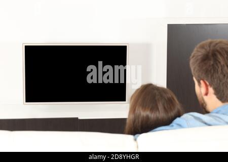 Vue arrière d'un couple en train de regarder la télévision avec blanc écran assis dans le canapé à la maison Banque D'Images