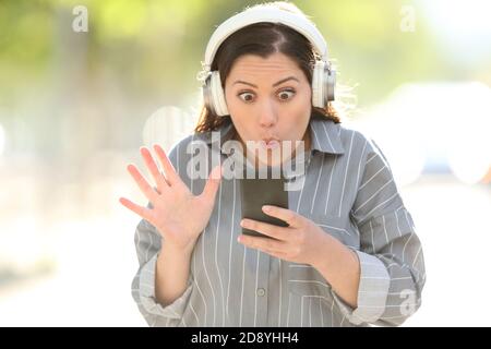 Vue avant portrait d'une femme stupéfaite portant un casque de trouver musique sur smartphone Banque D'Images