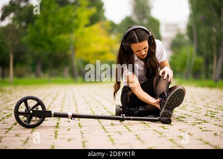 Femme d'affaires est en scooter de poussée dans le parc. Elle est tombée et tordue sa cheville. Banque D'Images