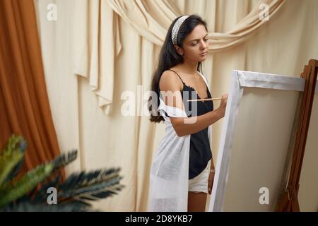 Jeune femme heureuse artiste devant le chevalet. Femme peinture en studio d'art Banque D'Images