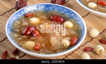 Gros plan de la soupe traditionnelle chinoise douce aux champignons blancs avec graines de lotus, dattes rouges (jujujube) et baies de carcajou (baie de goji, baie de gogyberry) sur le dos blanc Banque D'Images