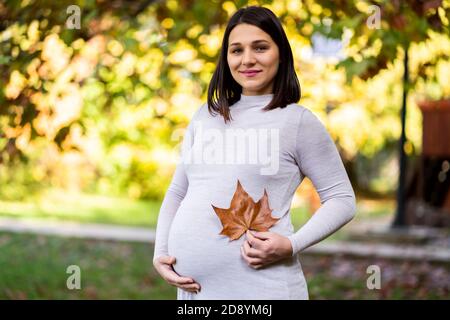 Portrait de la femme enceinte heureuse dans le parc en automne. Banque D'Images