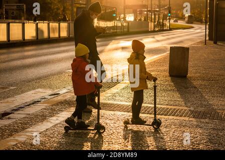 Père et deux filles avec masque traversent la rue À la station de métro Hradcanska avec des scooters pendant la période de quarantaine prévue À l'épidémie de COVID Banque D'Images