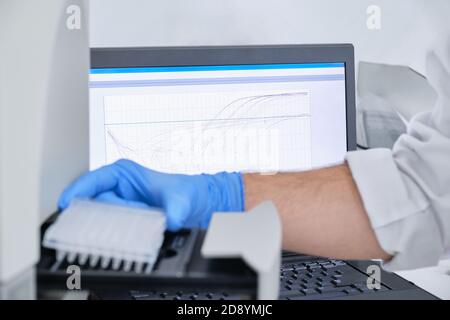 Un chercheur plaçant une plaque PCR sur le thermocycleur pour l'amplification de l'ADN. Courbe sur le moniteur derrière la mise au point. Test PCR du coronavirus. Banque D'Images