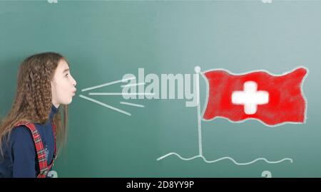 Une jeune fille qui soufflait sur le tableau scolaire est tirée sur le drapeau de la Suisse sur le tableau noir. Photo haute résolution. Profondeur de champ complète. Banque D'Images