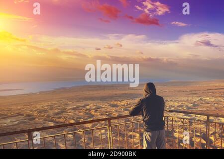 Jeune homme debout sur un point de vue sur la montagne (Masada) et regardant le lever du soleil sur la mer Morte. Région de la mer morte, Masada, Israël Banque D'Images