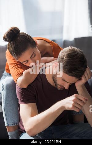 jeune femme penchée sur le dos d'un petit ami déprimé assis avec tête courbée Banque D'Images