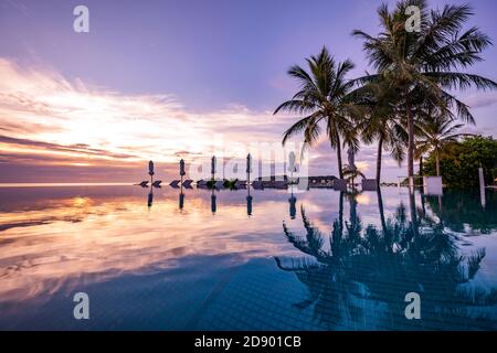 Magnifique piscine et coucher de soleil. Luxueux paysage tropical de plage, chaises longues et chaises longues et reflet de l'eau. Incroyable coucher de soleil baignade à l'infini Banque D'Images