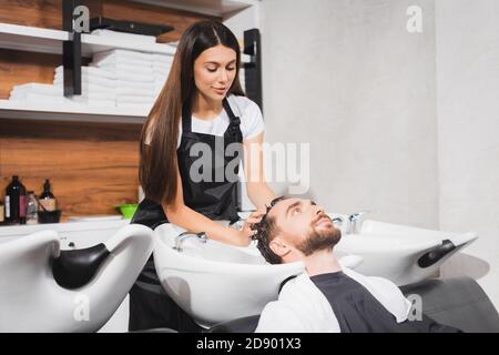 un jeune coiffeur lavant les cheveux de l'homme barbu dans un salon de beauté Banque D'Images