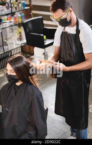 coiffeur dans l'équipement de protection regardant les cheveux de la femme dans masque médical Banque D'Images