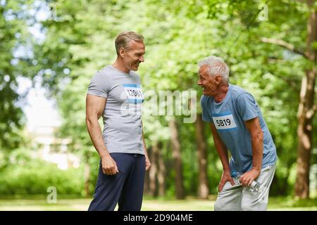 Portrait moyen long de deux hommes âgés qui y participent en course marathon d'été debout ensemble parler de quelque chose Banque D'Images