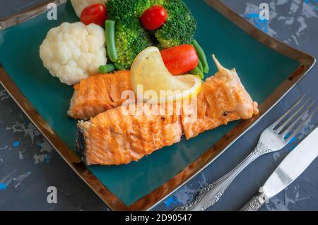 servir le saumon avec du citron, du brocoli et des légumes. Deux morceaux de saumon grillé sont servis sur une belle assiette. Banque D'Images