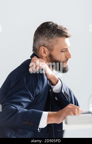 Vue latérale d'un homme d'affaires en costume qui ressent une douleur aux épaules avant-plan flou au bureau Banque D'Images