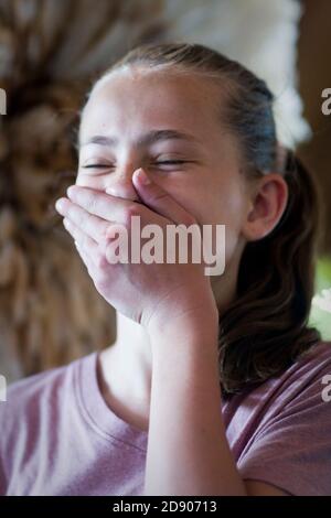 Une belle fille brune couvre sa bouche avec sa main comme elle rit Banque D'Images