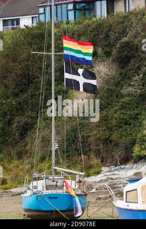 Un drapeau arc-en-ciel et un drapeau Cornouair St Piran volant du mât d'un bateau amarré sur le Gannel à Newquay en Cornouailles. Banque D'Images