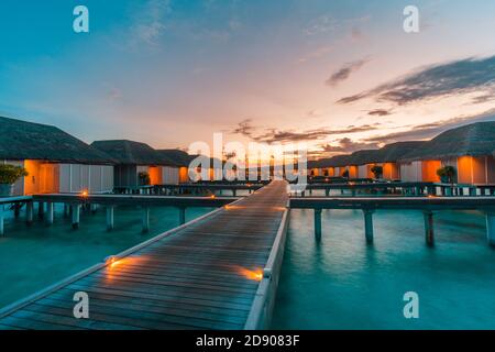 Îles Maldives et villas aquatiques. Île dans l'océan, villas sur l'eau à l'époque coucher de soleil avec lumières à DEL et ciel crépuscule. Resort de luxe, bungalow sur jetée Banque D'Images