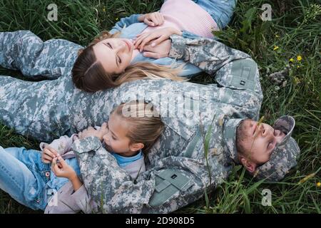 Vue en hauteur du militaire qui se repose et embrasse sa femme et sa fille, tout en étant allongé sur l'herbe Banque D'Images