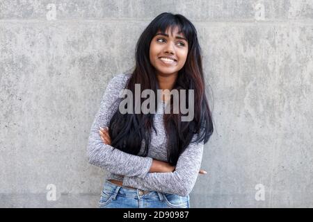 Portrait d'une jeune femme indienne heureuse avec les armes croisées mur gris Banque D'Images