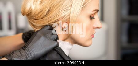 Mains de coiffeur faire la préparation avant de donner la coupe de cheveux à jeune femme blonde au salon de beauté Banque D'Images