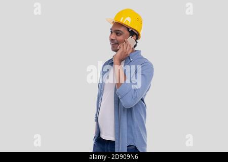 Travailleur de la construction parlant au téléphone. Téléphone de maintien de l'architecte. Casque dur jaune. Homme isolé parlant au téléphone. Homme ayant un appel au travail Banque D'Images
