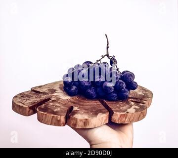 bouquet de raisins bleu foncé en gouttes d'eau sur une planche en bois à la main sur fond blanc Banque D'Images