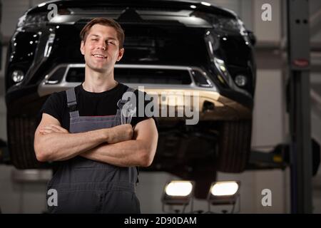 portrait d'un agréable mécanicien d'auto posant à la caméra, souriant. automobile en arrière-plan Banque D'Images