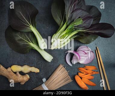 Ingrédients pour faire sauter : légumes verts bok choy, gingembre, nouilles soba, carottes et oignons violets. Banque D'Images