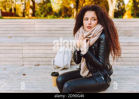 Femme solitaire en colère portant un pull confortable et chaud et une écharpe asseyez-vous sur le banc dans le parc à l'automne ensoleillé jour Banque D'Images