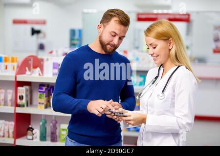 le pharmacien amical caucasien a une belle conversation avec un client, aide à trouver un médicament, pose des questions sur les symptômes et de ce qui est il souffre Banque D'Images