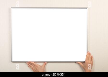 Personne accroche un cadre au mur. Espace vide pour votre photo, photo, lettre de gratitude, design ou logo. Maquette horizontale. Cadre de maquette vide Banque D'Images