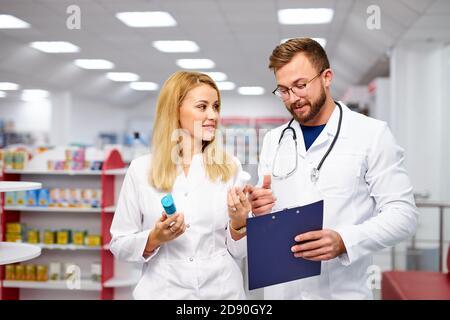 une équipe de jeunes chimistes ou buveurs caucasiens discutant des médicaments, vérifier les indications médicales, dans les robes médicales blanches, sur le lieu de travail Banque D'Images