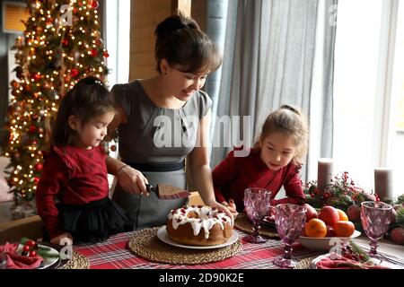 Une femme coupe une tarte pour Noël. Les enfants attendent une portion de tarte à la table de fête. Banque D'Images