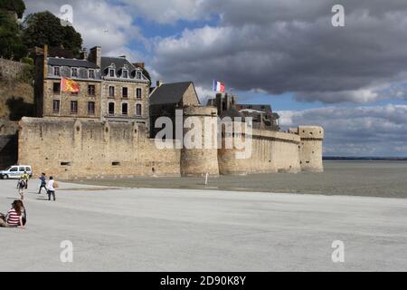 le mur renforcé et une maison et la route à l'entrée du mont saint-michel en normandie, france en été avec un ciel nuageux Banque D'Images