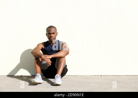 Portrait du jeune homme afro-américain sportif assis sur le sol par mur Banque D'Images