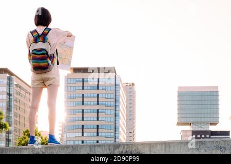 vue arrière d'une jeune fille voyageur avec sac à dos recherche d'une carte en face de la ville, concept de la jeunesse et le mode de vie nomade, espace de copie pour le texte Banque D'Images