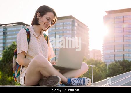 jeune voyageur heureuse femme avec sac à dos assis dans la ville dactylographiant sur son ordinateur, concept de la technologie, jeune et numérique nomade style de vie, copie sp Banque D'Images