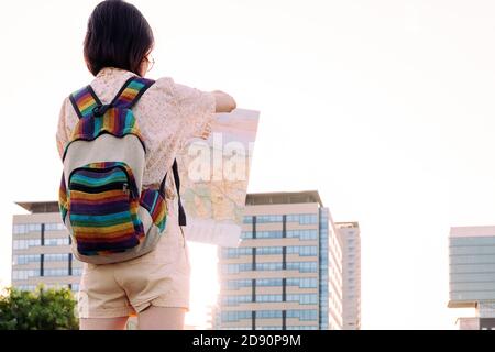 vue arrière d'une jeune femme voyageur avec sac à dos à la recherche d'une carte en face de la ville, concept de la jeunesse et le mode de vie nomade, espace de copie pour le texte Banque D'Images